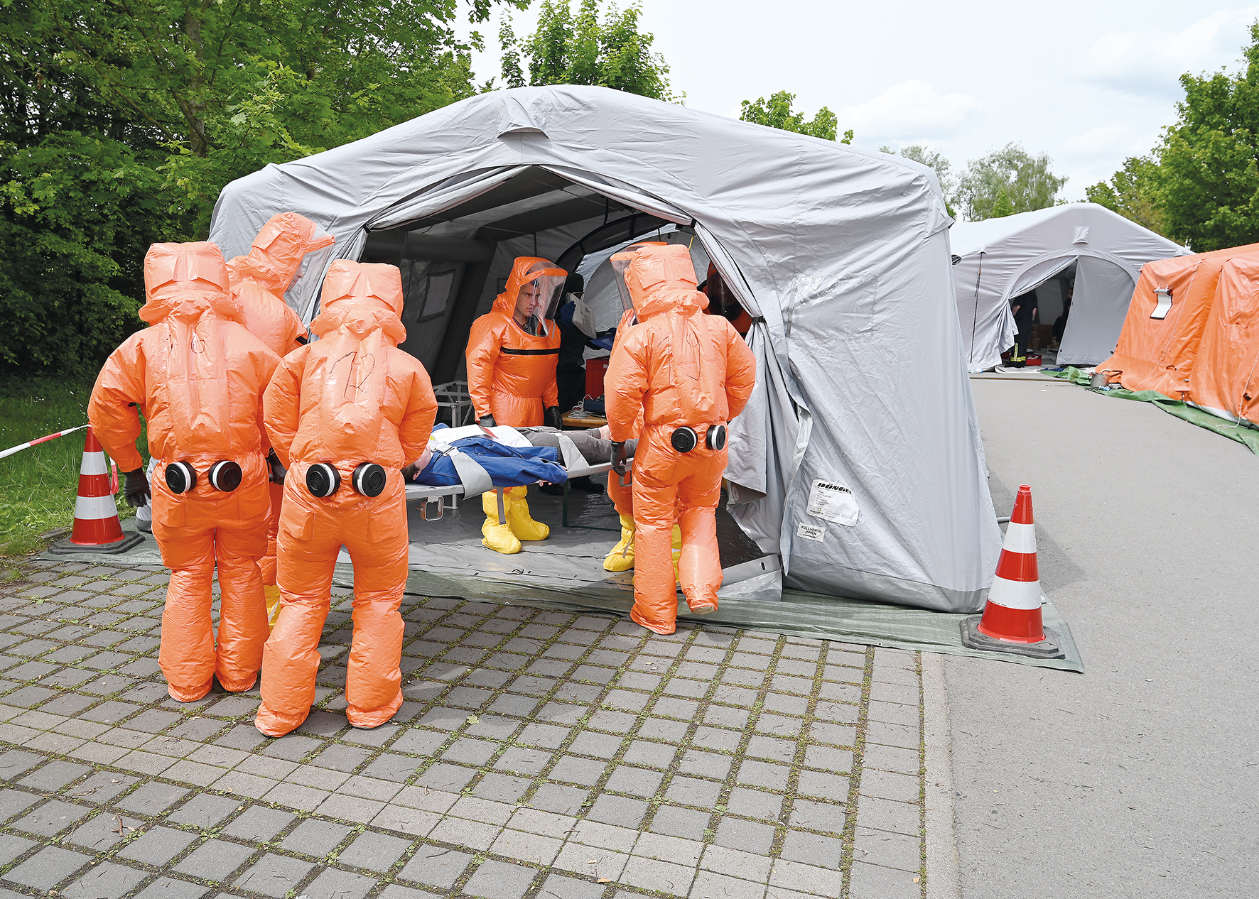 Mehrere Menschen mit Chemikalienschutzanzug VenION® stehen vor Zelt auf der Straße